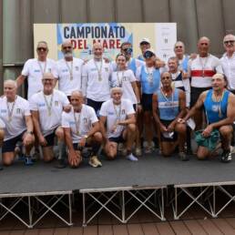 Foto di gruppo dei canottieri con le medaglie davanti al pannello dei Campionati del Mare 2026 a Genova Pra’